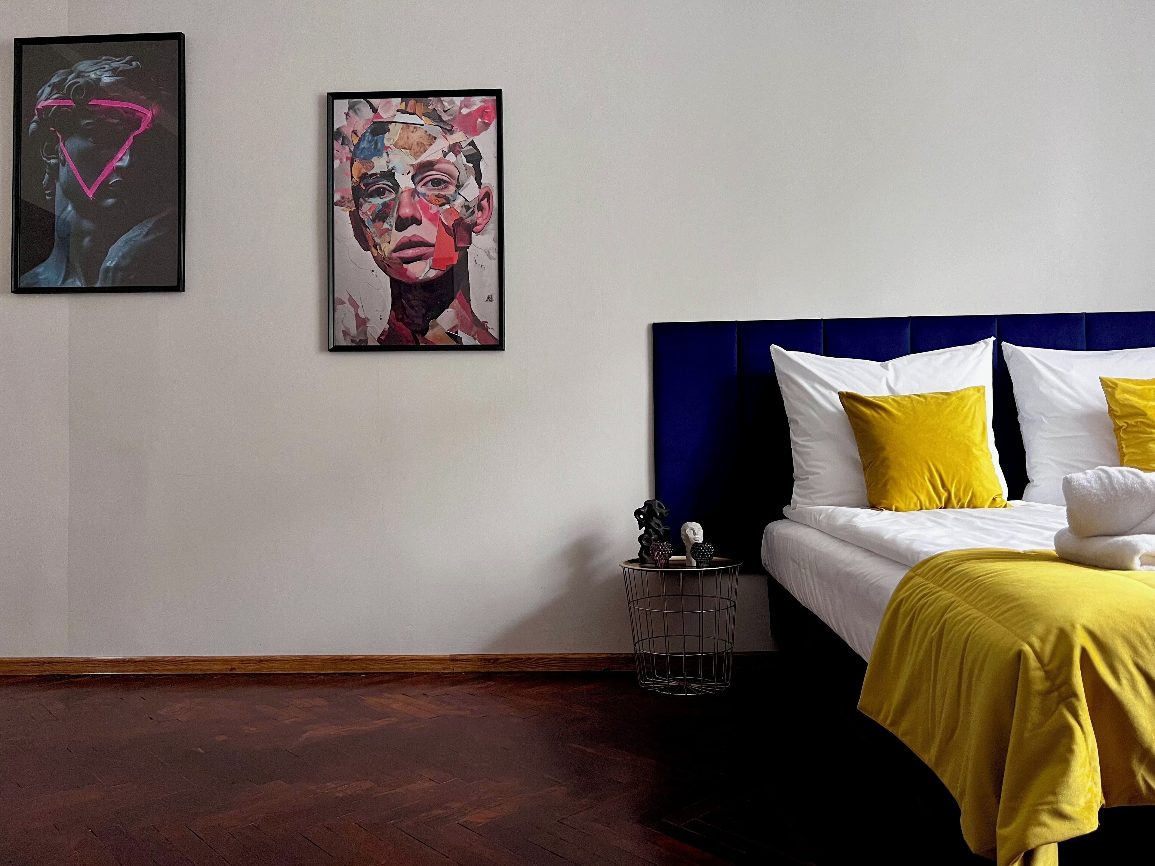 A modern bedroom with a bed, a bedside table, and two artworks on the wall.