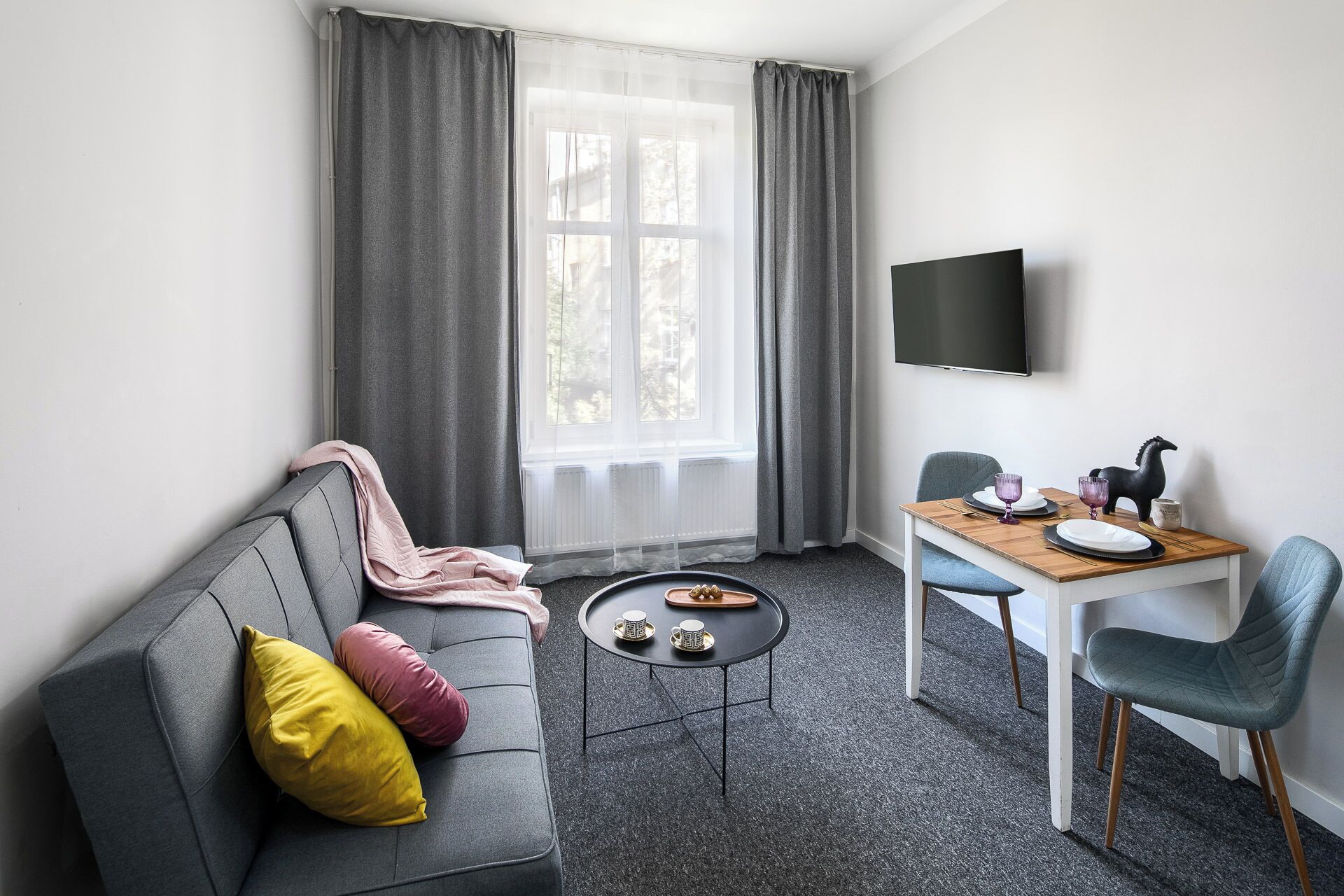Un salon moderne avec un canapé gris, une petite table ronde et une table à manger avec des chaises.