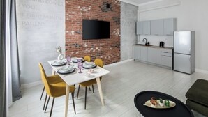 Una cocina moderna con un televisor de pantalla plana, una zona de comedor con sillas amarillas y una pequeña mesa preparada para dos.