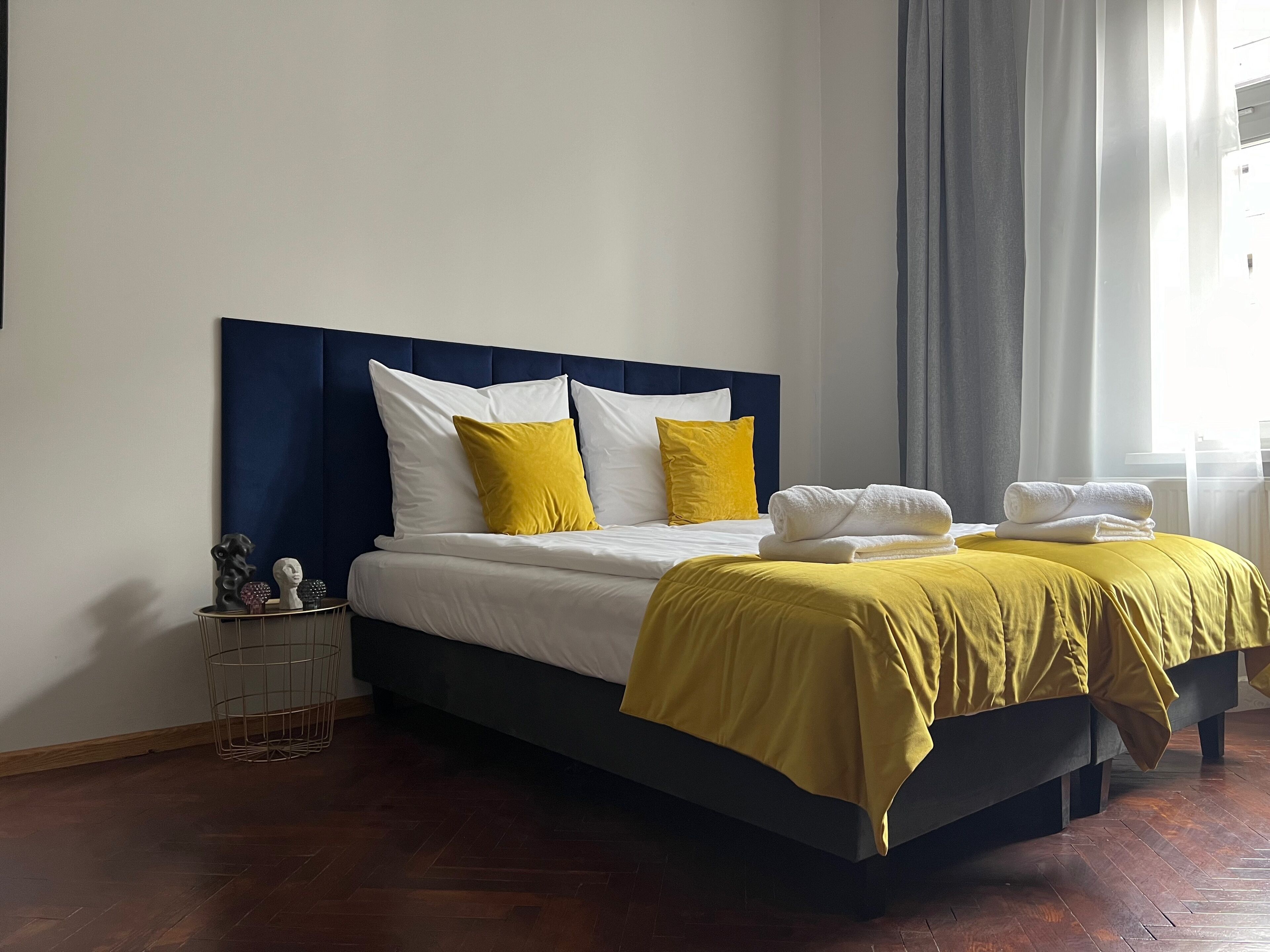 A neatly made bed with white and yellow bedding, a dark headboard, and a wooden floor.