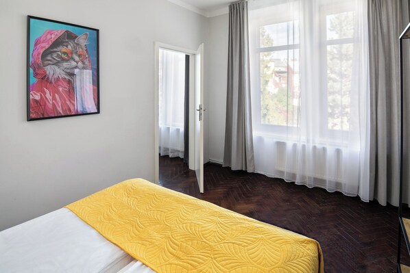A bedroom with a bed, a painting, and a window with curtains.