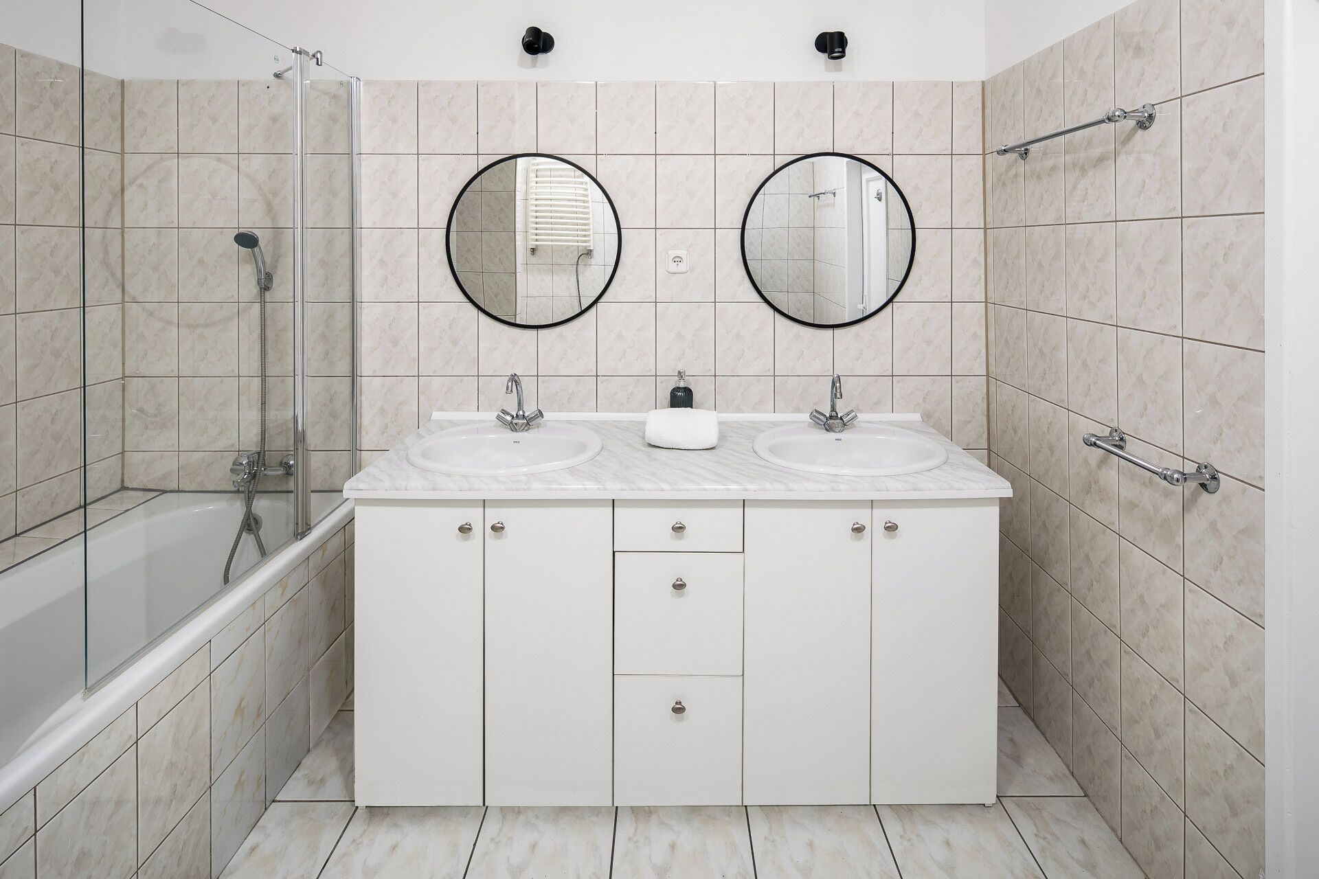 Un baño moderno con dos lavamanos, cabina de ducha de vidrio y tocador blanco con armarios.