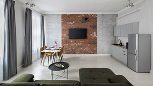 Un espacio moderno de estar con zona de comedor, cocina y televisor grande montado en una pared de ladrillo.