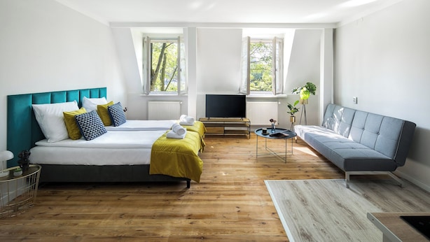 Un dormitorio moderno con dos camas, un sofá, un televisor y ventanas amplias.
