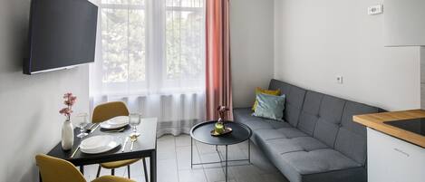 Una sala de estar moderna con un sofá gris, una mesa de comedor con sillas amarillas y un televisor montado en la pared.