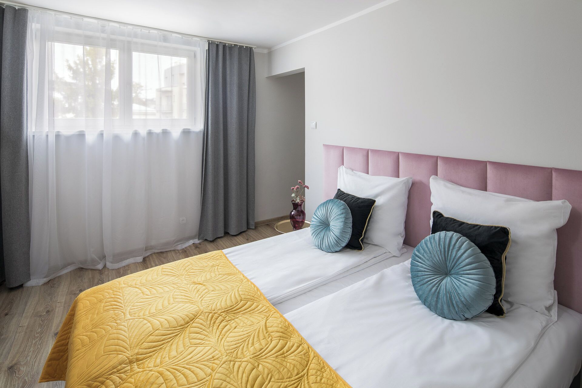 A hotel room with a bed, a bedside table, and a window with curtains.