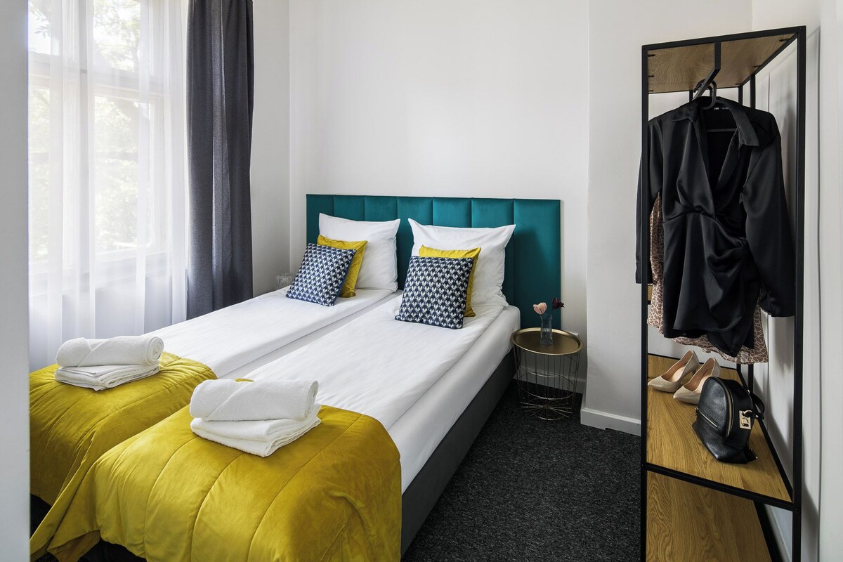 A hotel room with a bed, two pillows, a bedside table, a mirror, and a coat rack.