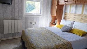 A bedroom with a bed, wooden headboard, window, and a TV mounted on the wall. - Lovely Lodge Next To The Mansion House Llansteffan (Carmarthen)