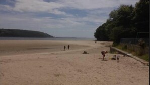A beach with a sandy shore, a few people, and some greenery in the background. - Lovely Lodge Next To The Mansion House Llansteffan (Carmarthen)