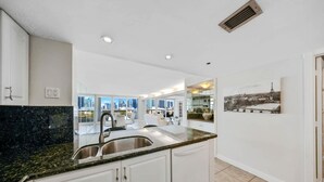 Cozinha moderna com armários brancos, bancada de granito e uma grande janela com vista para a cidade.