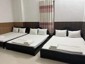 A hotel room with two single beds, each with a black frame and white bedding. There is a window with a striped curtain, and the walls are tiled in a brown and white pattern. - Kien An Hotel (Can Tho)