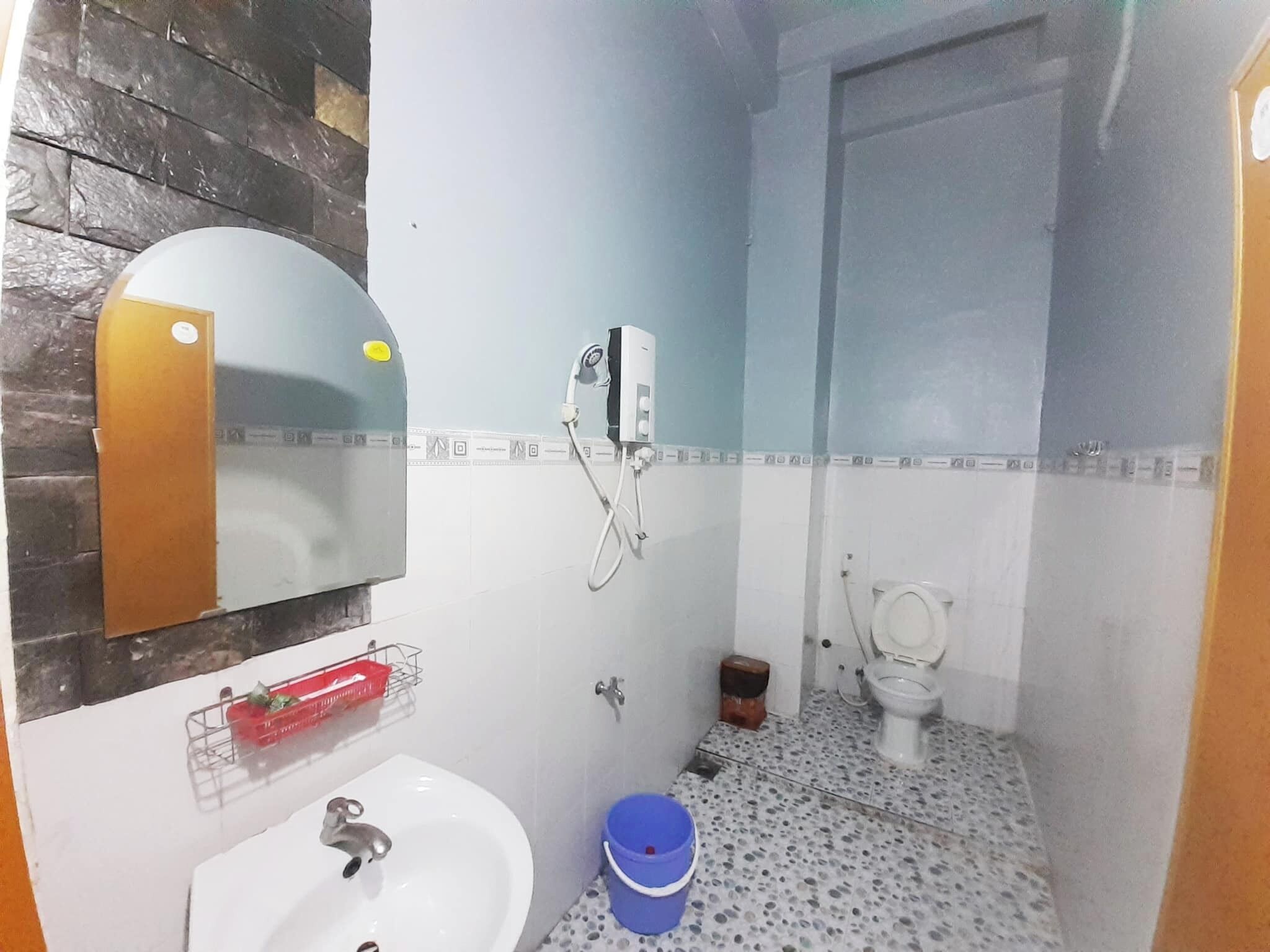 A bathroom with a sink, mirror, shower, toilet, and a blue bucket.