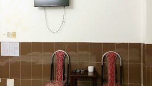 A room with a flat-screen TV mounted on the wall, two wooden chairs with red cushions, a small table with a cup, and a tiled floor. - Kien An Hotel (Can Tho)