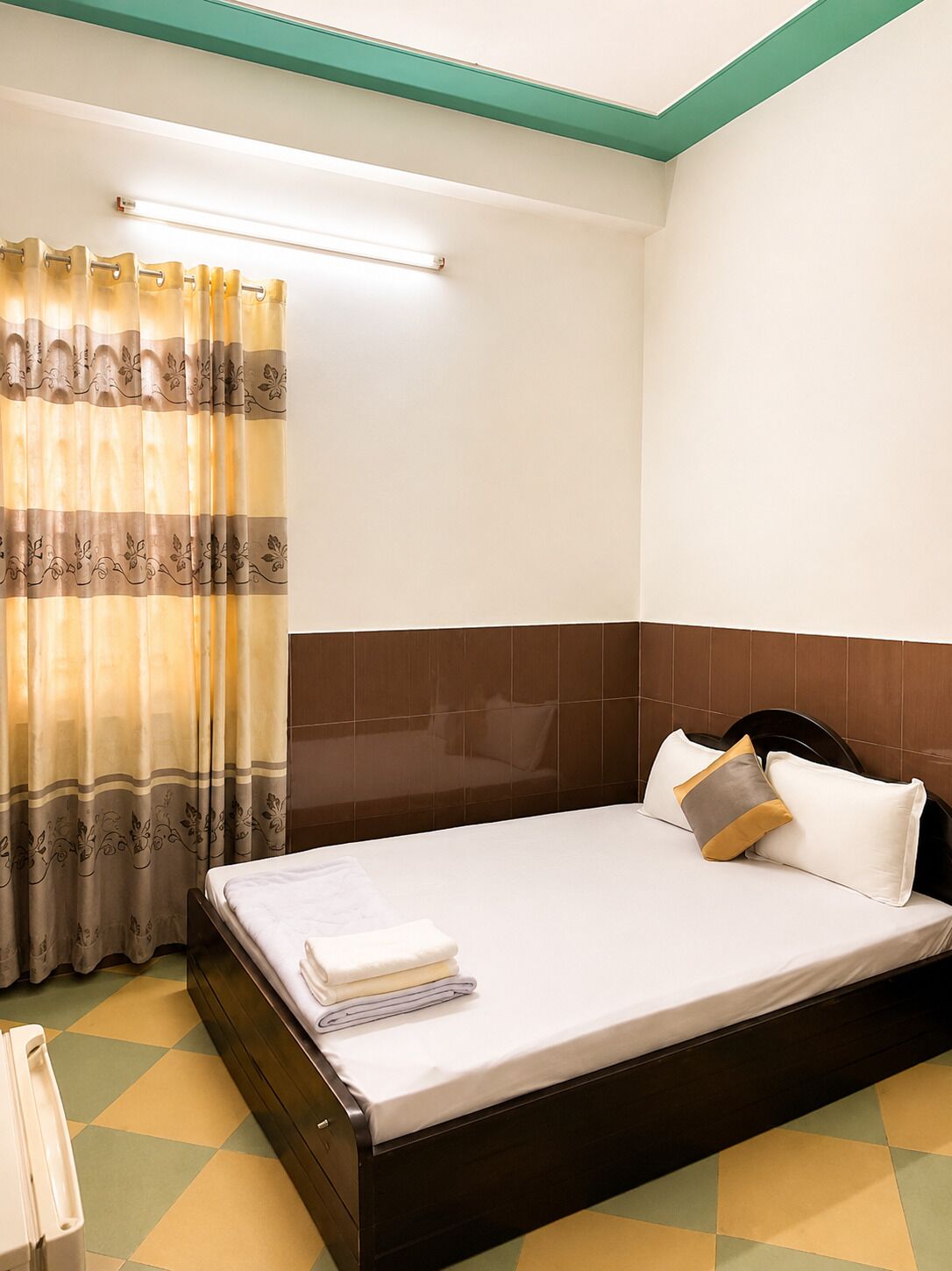 A hotel room with a bed, a nightstand, a lamp, and a window with curtains.