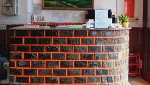 A reception area with a brick counter, a framed landscape painting, and a small potted plant. - Kien An Hotel (Can Tho)