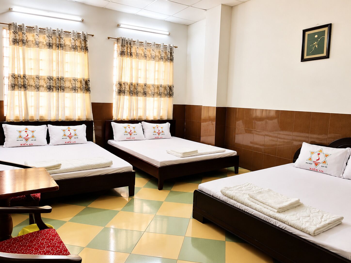 A hotel room with two single beds, a wooden headboard, a checkered floor, and a table with chairs.