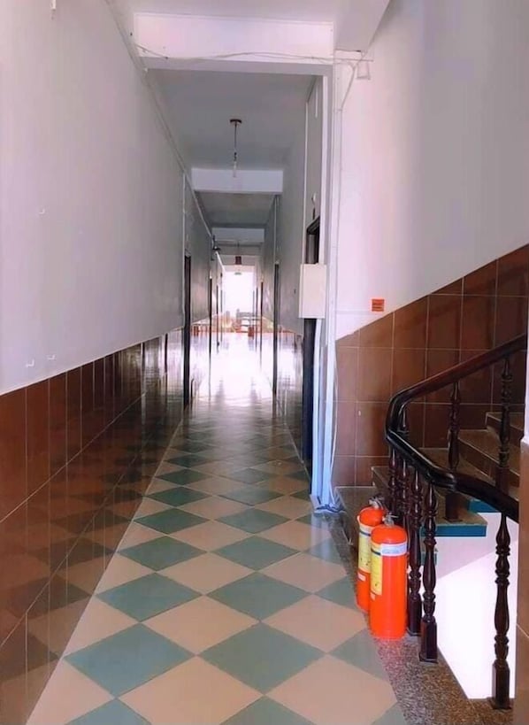 A hallway with a checkered floor, a staircase on the right, and a door at the end.