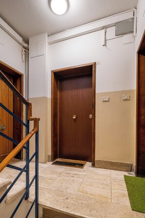 A hallway with a wooden door, a blue handrail, and a green mat at the entrance. - Porta Mascarella Apartment by Wonderful Italy (Bologna)