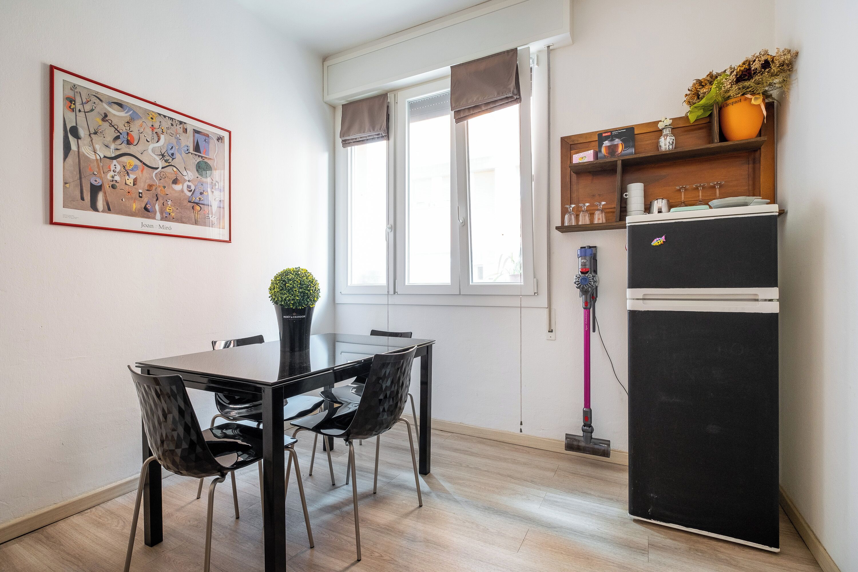 Une petite cuisine équipée d’une table à manger, de chaises, d’un réfrigérateur et d’une fenêtre avec des rideaux.