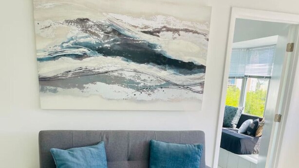 Un sofá gris con cojines azules, una orquídea blanca sobre una mesa de mármol y un cuadro abstracto grande en la pared.