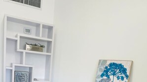 Un escritorio blanco con un cuadro floral azul, un pequeño jarrón azul y una cita enmarcada sobre un estante blanco.