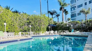 Una piscina con borde de azulejos, rodeada por una valla blanca y palmeras.