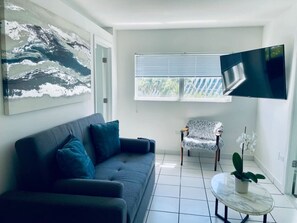 Una sala de estar moderna con un sofá gris, una silla blanca, un televisor de pantalla plana y una orquídea en maceta.