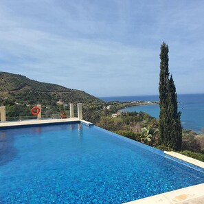 Una piscina azul cristalina con vistas a un paisaje costero y una colina al fondo.
