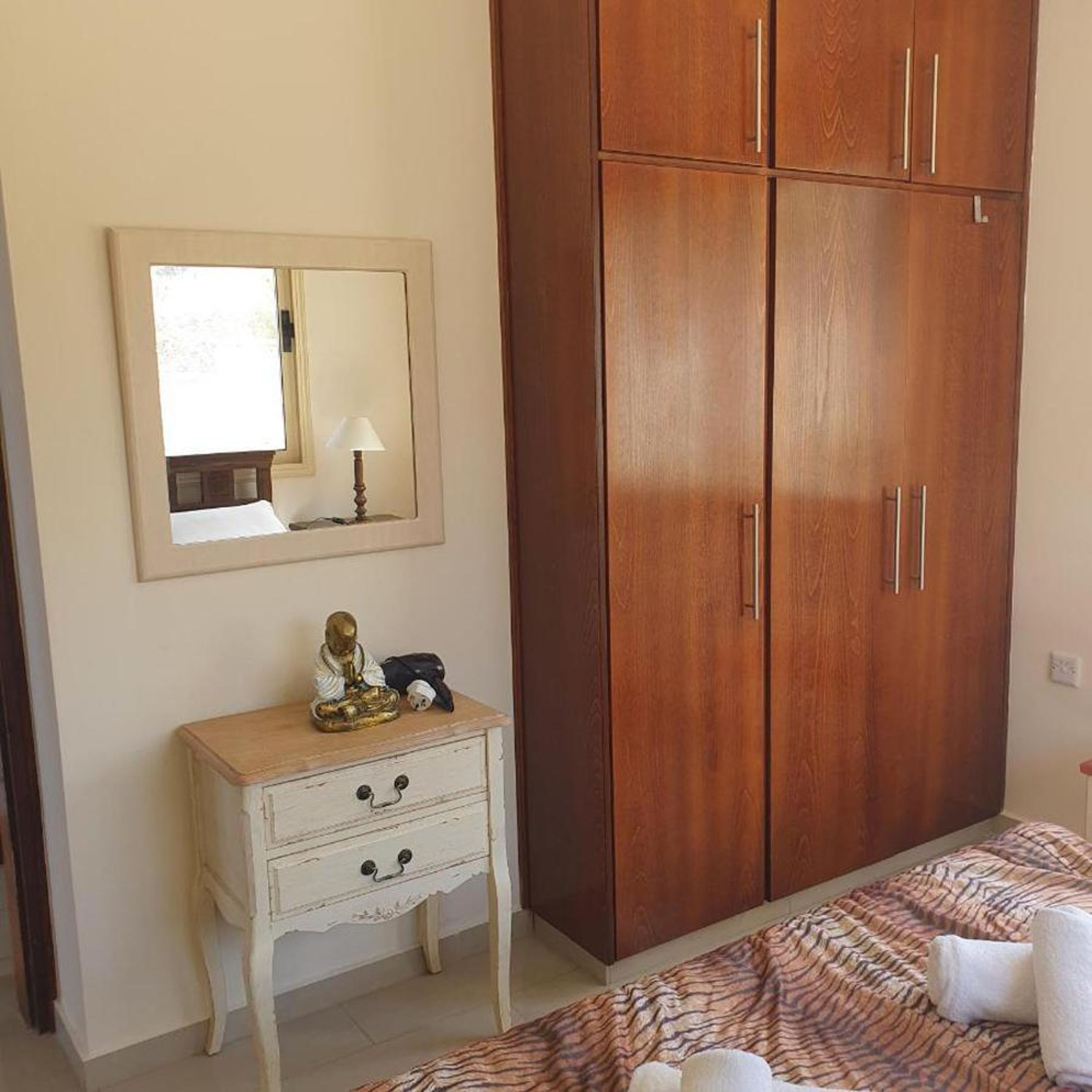 A bedroom with a wooden wardrobe, a bedside table with a lamp, and a bed with a patterned bedspread.