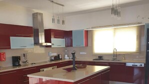 A modern kitchen with a central island, red cabinetry, and a large window providing natural light. - Villa Aquavitus in Pachyammos (Pomos)