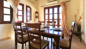 A dining area with a wooden table set for four, surrounded by chairs with cushioned seats. - Villa River View in Peristerona (Peristerona)