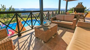 A covered outdoor seating area with wicker furniture, a pool, and a grill. - Villa River View in Peristerona (Peristerona)