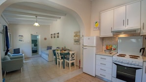 Une cuisine compacte avec des meubles blancs, une cuisinière et un réfrigérateur. On y trouve également un coin repas avec une table et des chaises.