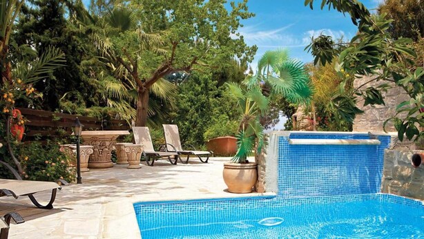 Una piscina con bordes de azulejos, rodeada de tumbonas y plantas en macetas.