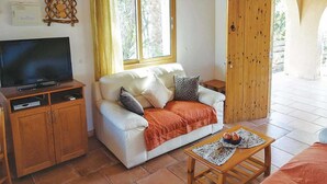 Una sala de estar con sofá, televisor, aparador de madera y una ventana con cortinas.