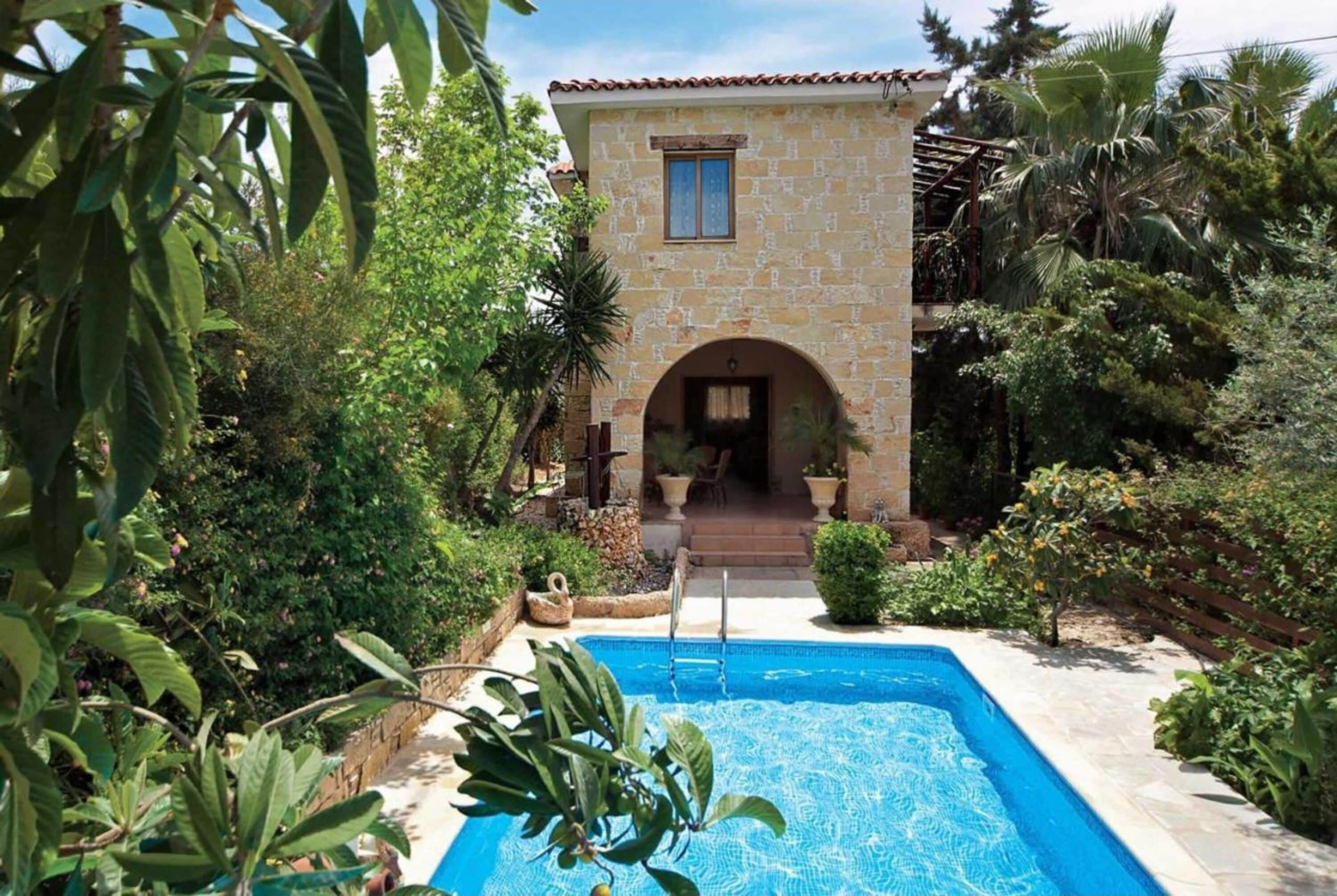 Ein Gebäude aus Stein mit Pool und üppiger Bepflanzung.