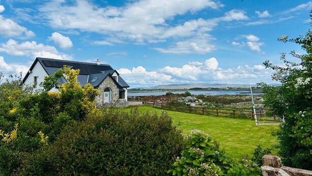 Une maison avec une façade en pierre, un toit en pente et une vue sur un lac et des montagnes au loin.