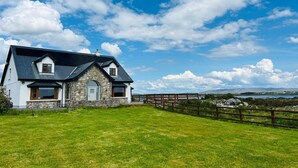 Une maison à deux étages avec une façade en pierre et une grande pelouse devant.