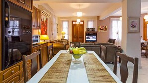 A dining area with a table set for four, a fruit bowl, and a kitchen with a refrigerator and microwave. - Villa Irene Palace in Peristerona (Peristerona)
