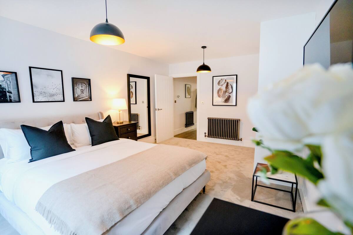 Une chambre à coucher moderne avec un grand lit, des tables de chevet, un radiateur et des œuvres d’art encadrées accrochées aux murs.