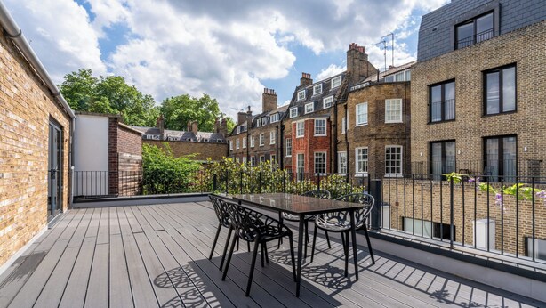 A wooden deck with a table and chairs, surrounded by brick buildings and a clear sky. - Be London - The Bloomsbury Residences (London)