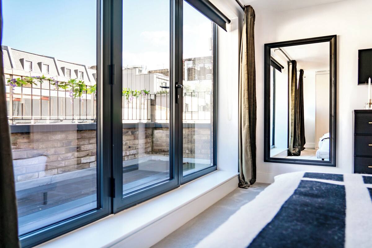 Une chambre moderne avec de grandes fenêtres, un tapis rayé noir et blanc et un miroir au mur.