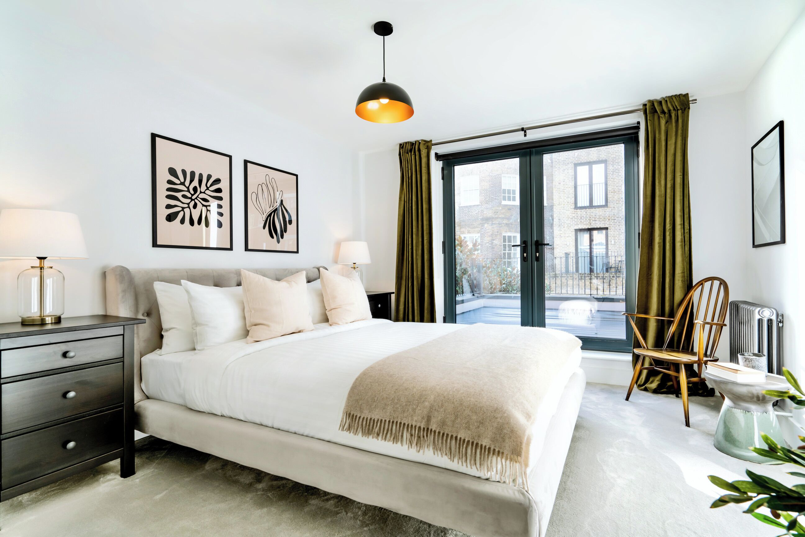A modern bedroom with a large bed, a bedside table, a chair, and a view of the outside.