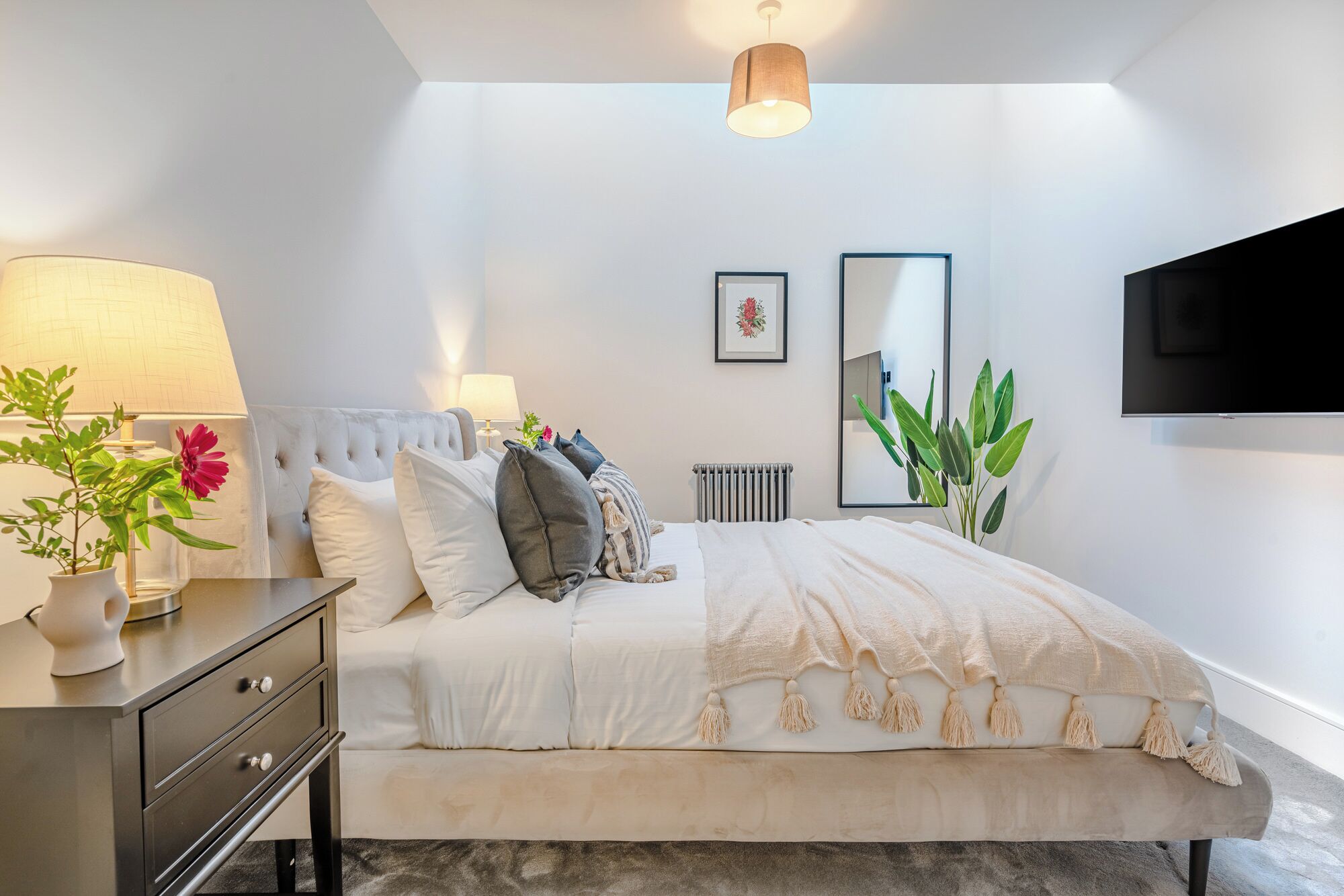 A modern bedroom with a bed, bedside tables, a radiator, and a large mirror.