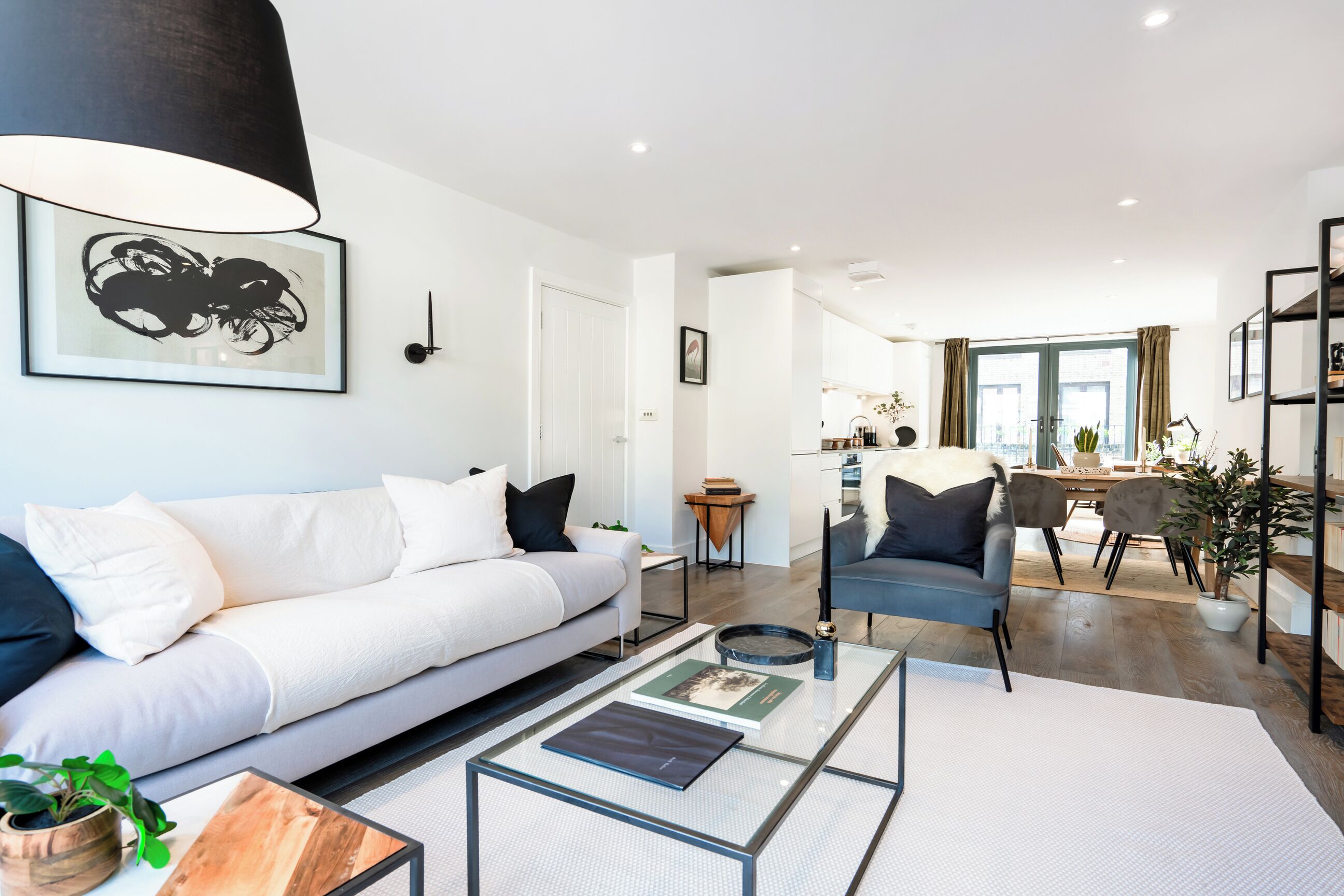 A modern living room with a white sofa, a glass coffee table, and a dining area with a table and chairs.