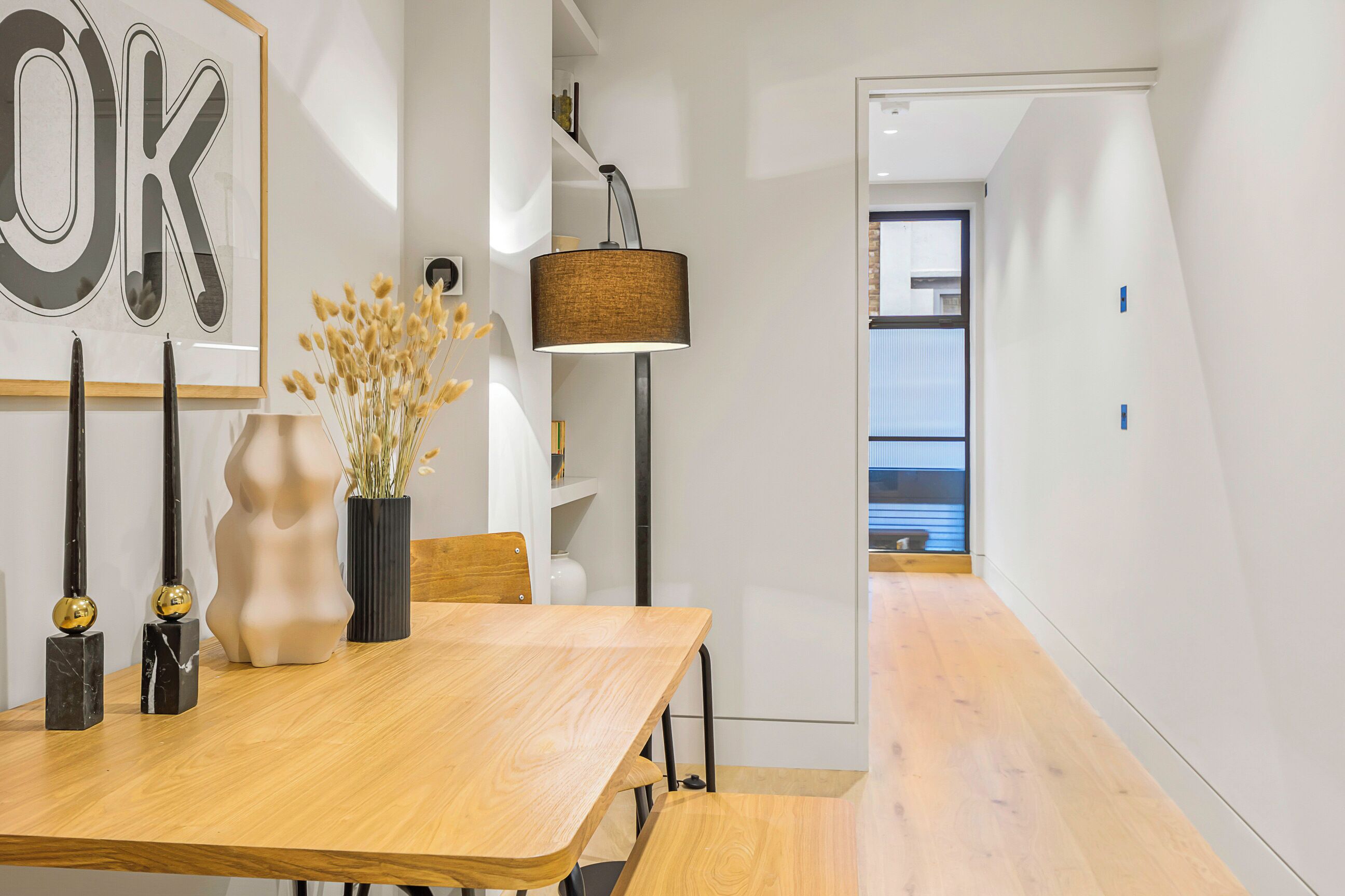 Een moderne eetruimte met een houten tafel, decoratieve items in zwart en goud, een vaas met gedroogde bloemen en een vloerlamp.