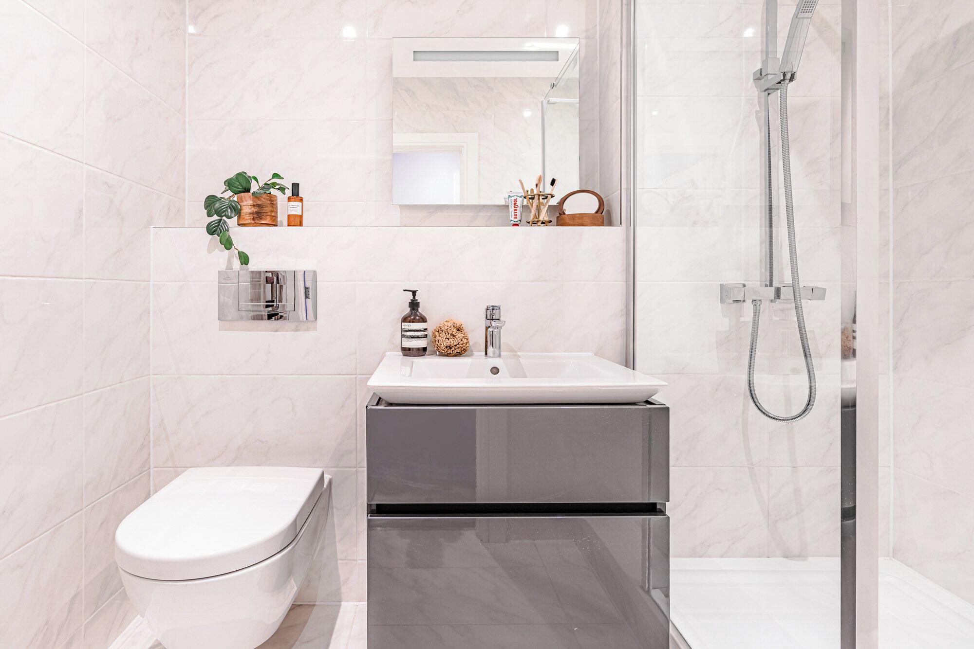 A modern bathroom with a white toilet, a sink with a mirror above it, and a shower with a handheld hose.