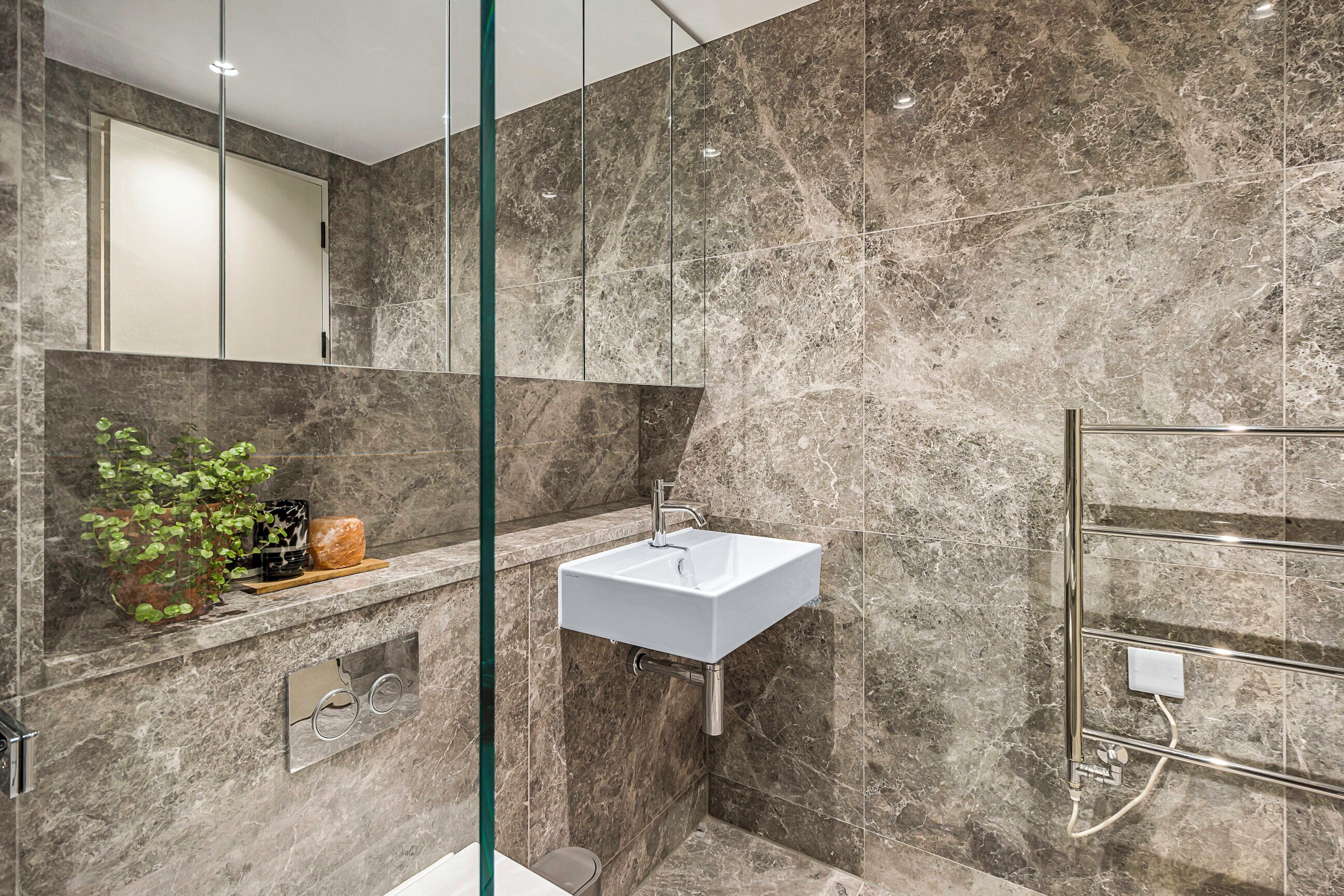 A modern bathroom with a marble sink, a glass shower enclosure, and a marble-tiled wall.