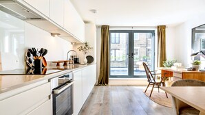 A modern kitchen with white cabinets, a wooden countertop, and a dining area with a table and chairs. - Be London - The Bloomsbury Residences (London)