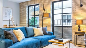 A modern living room with a blue sofa, a wooden coffee table, and a brick wall. - Be London - The Bloomsbury Residences (London)